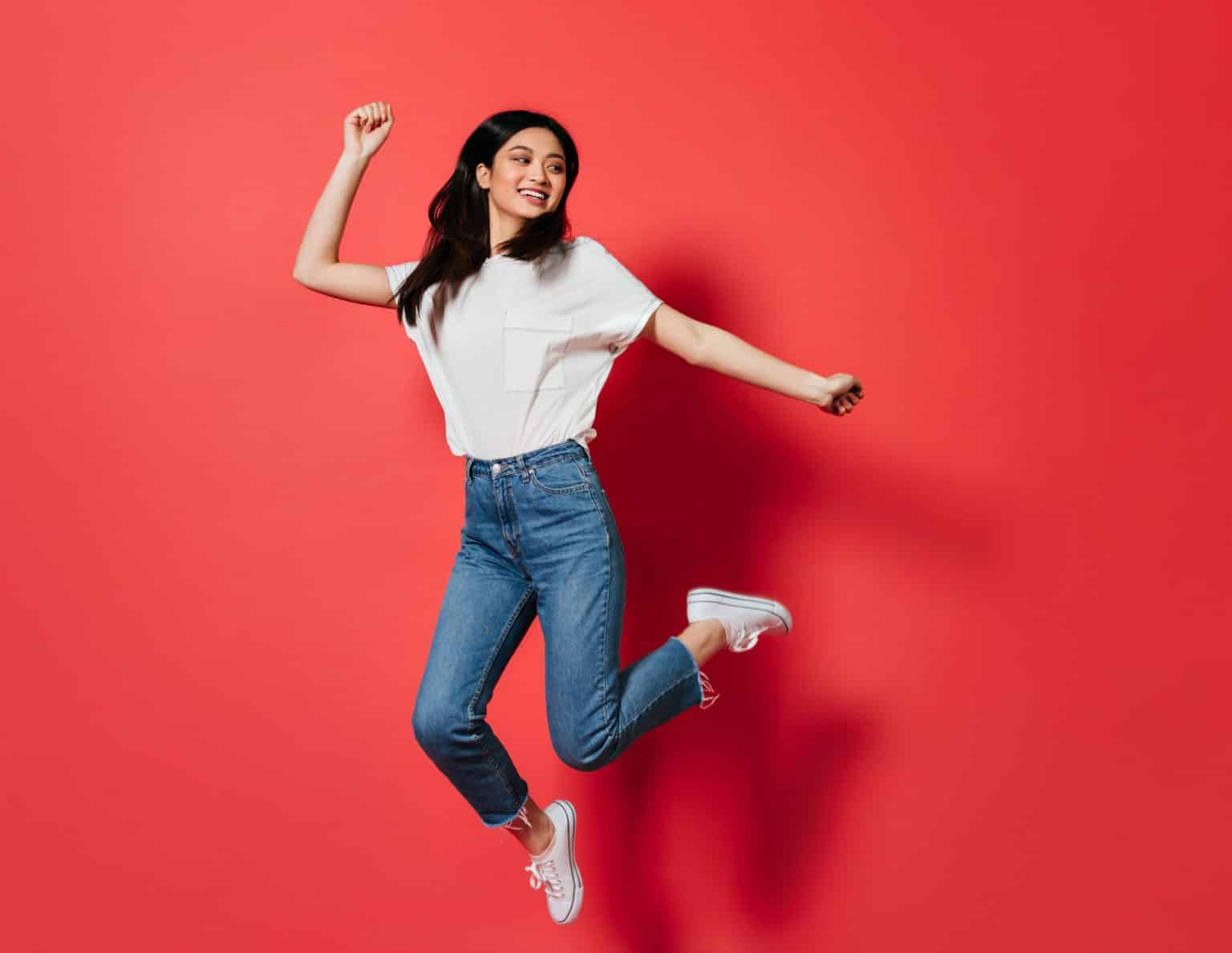 mischievous woman white t shirt jeans jumping red wall 2